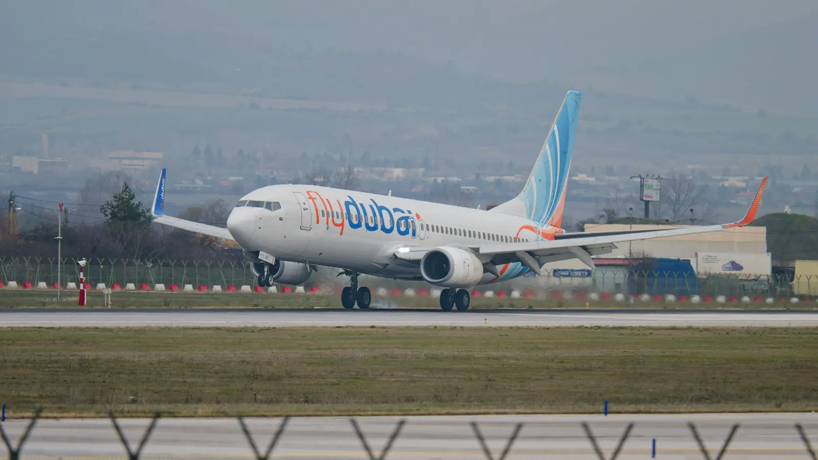 A flydubai Boeing 737 on a runway, with the airline name on the fuselage and a blue and orange tail.